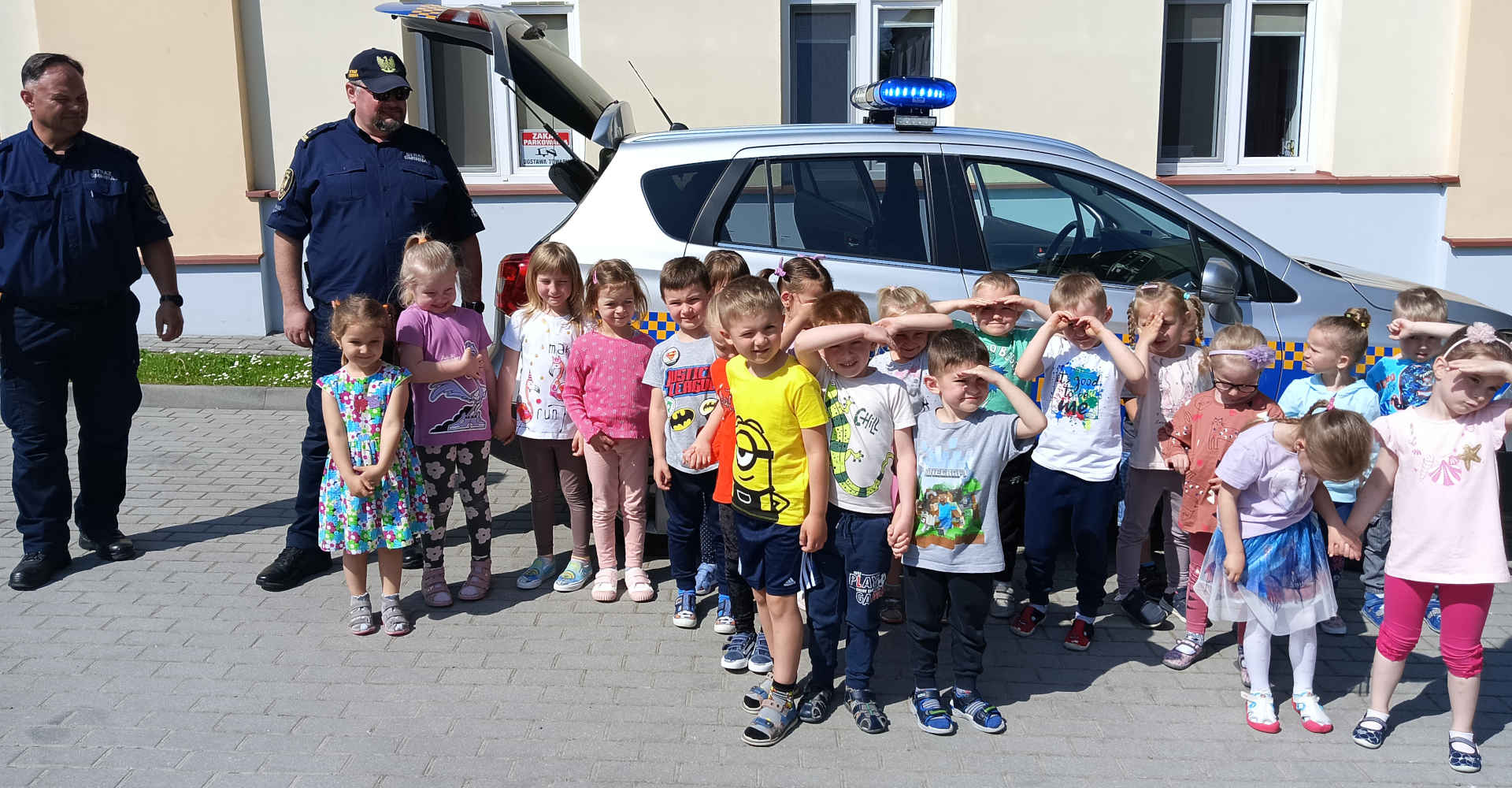 Zdjęcie grupowe dzieci wraz ze strażnikami gminnymi, w tle samochodów straży gminnej